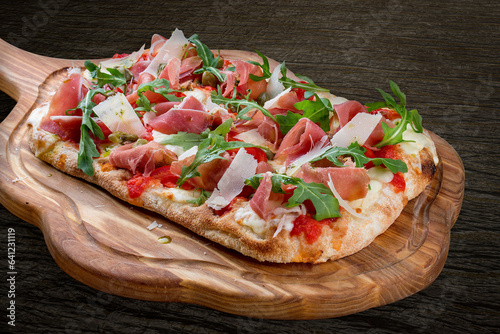 Sorrentina pizza with prosciutto, arugula, capers, pelati sauce, pesto. Roman pizza rectangular on wood background