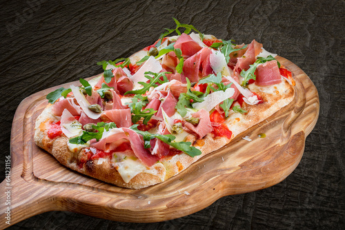 Sorrentina pizza with prosciutto, arugula, capers, pelati sauce, pesto. Roman pizza rectangular on wood background photo