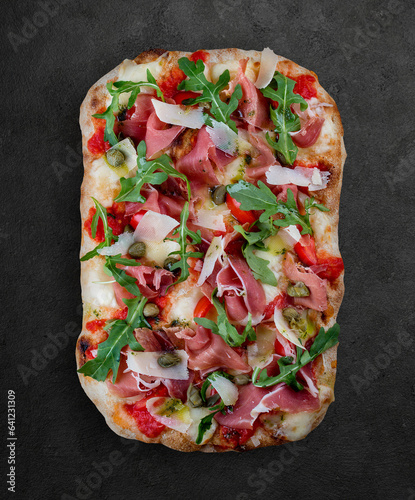 Sorrentina pizza with prosciutto, arugula, capers, pelati sauce, pesto. Roman pizza rectangular on dark background photo