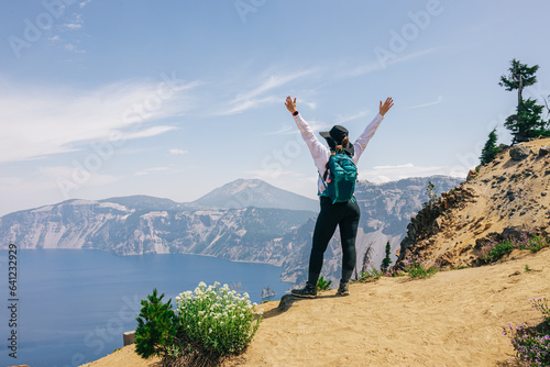 Woman hiker standing with her hands rised with a view to a picturesque lake © Diana Vyshniakova