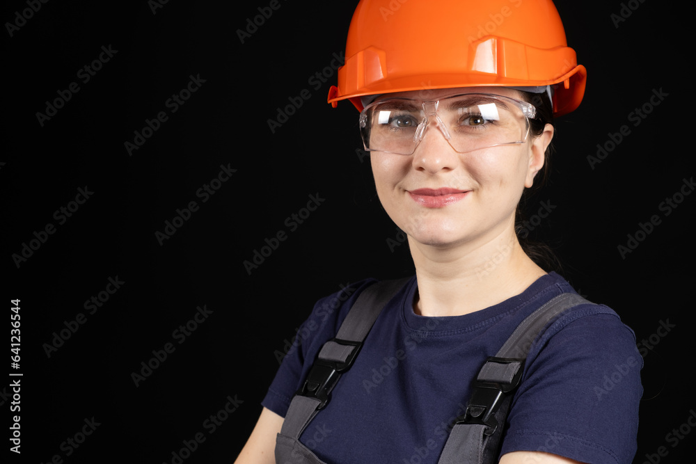 A woman in a protective helmet, glasses and overalls on a black background with space for text. A woman in a protective helmet, glasses and overalls on a black background with space for text.