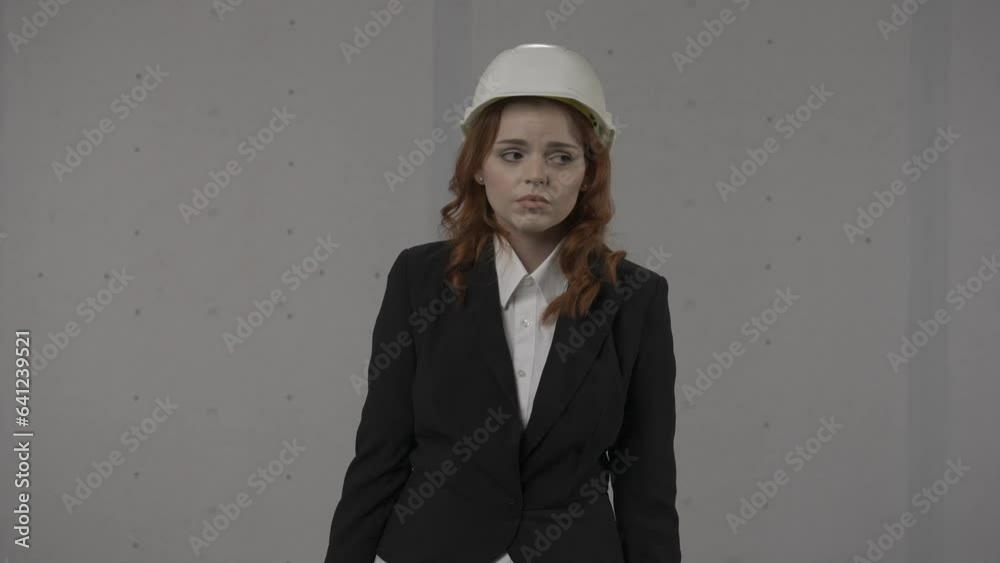 Embarrassed woman covering her mouth with palm, oops. Woman architect in a helmet and business suit in the studio on a gray background. HDR BT2020 HLG Material. Embarrassed woman covering her mouth with palm, oops. Woman architect in a helmet and business suit in the studio on a gray background. HDR BT2020 HLG Material.