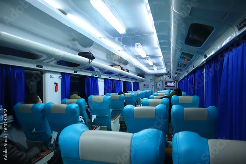 Executive class train interior with blue seats, armrests, luggage racks, monitor screens, air conditioning, and lights that extend on the ceiling