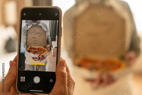 Shooting on the phone, a box of pizza in the form of a heart in the hands of a man proposing marriage