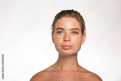 Pretty girl with freckles looking at the camera with her hair tied up in front of the camera on a white background