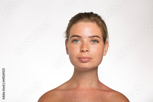 Pretty girl with freckles looking at the camera with her hair tied up in front of the camera on a white background