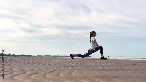 A young girl is doing sports on the seashore. Squats. Stretching. Yoga. Sports exercises. Charging. Warm-up. Sportswear. A person does sports.
