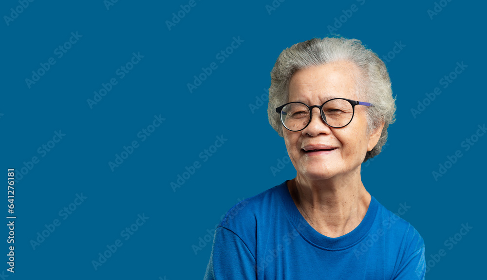 Beautiful senior woman with short white hair and glasses smiles at the camera while standing against a blue background. Beautiful senior woman with short white hair and glasses smiles at the camera while standing against a blue background.
