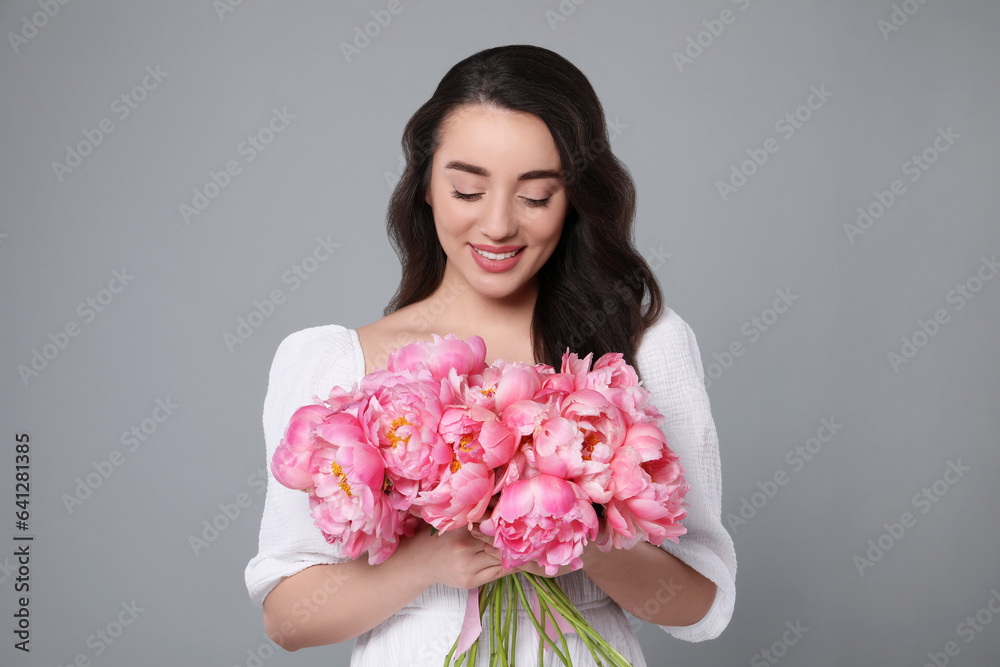 Beautiful young woman with bouquet of pink peonies on grey background