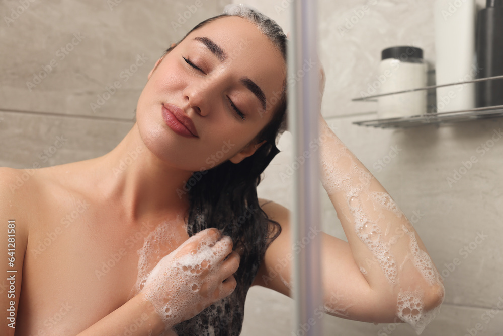 Naklejka premium Beautiful woman washing hair with shampoo in shower