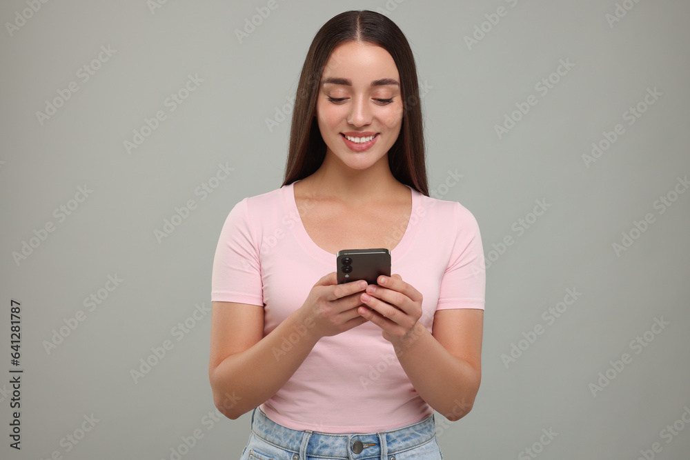 Happy young woman using smartphone on light grey background Happy young woman using smartphone on light grey background