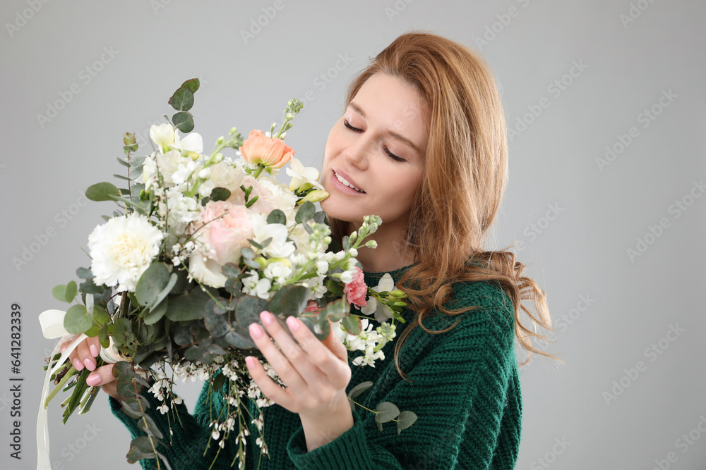 Beautiful woman with bouquet of flowers on grey background
