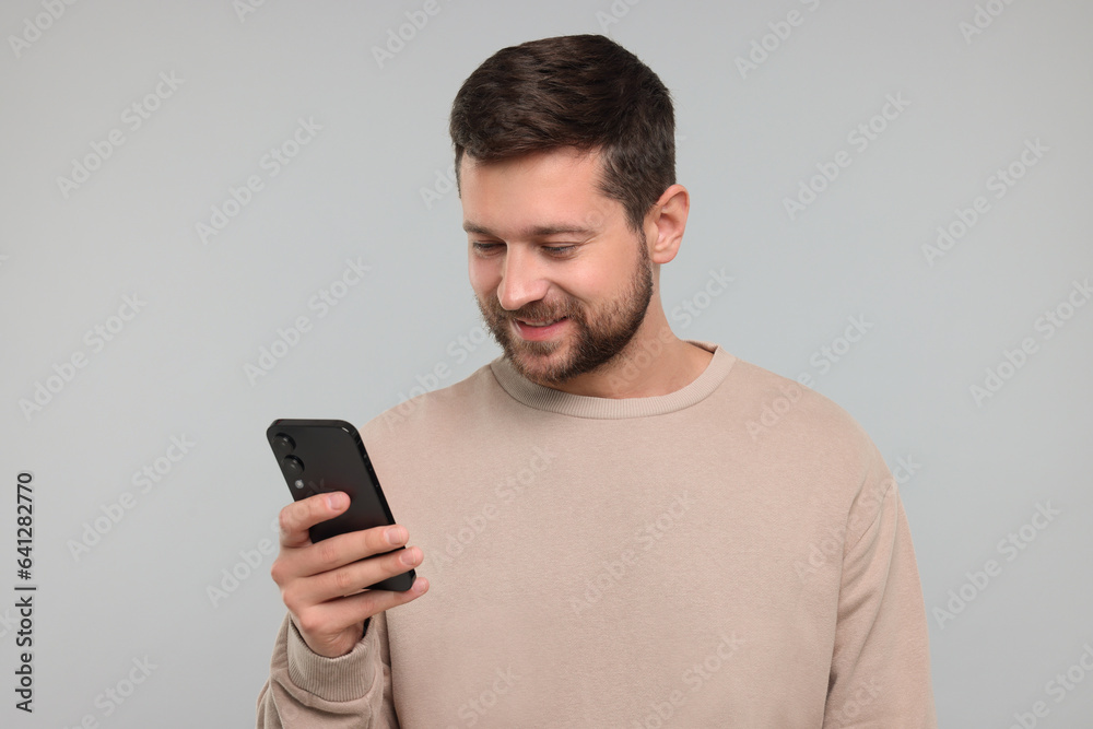 Happy man using smartphone on light grey background Happy man using smartphone on light grey background