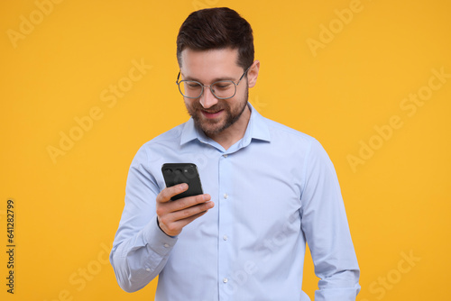 Happy man using smartphone on yellow background © New Africa