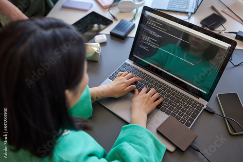 Focus on hands of young female student in green sweatshirt typing on laptop keyboard while analyzing and decoding data on screen
