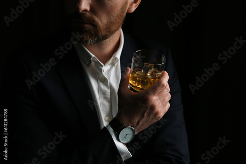 Man holding glass of whiskey with ice cubes on black background, closeup. Space for text