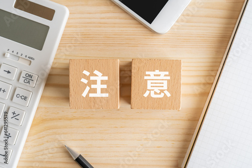 注意と書かれたブロック、電卓、スマホ