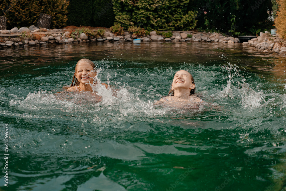 Two little girls swim and indulge in swimsuits in a lake with cold water on a hot summer day
