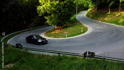 drone shot of a car driving dynamically through a sharp turn in a green forest in summer