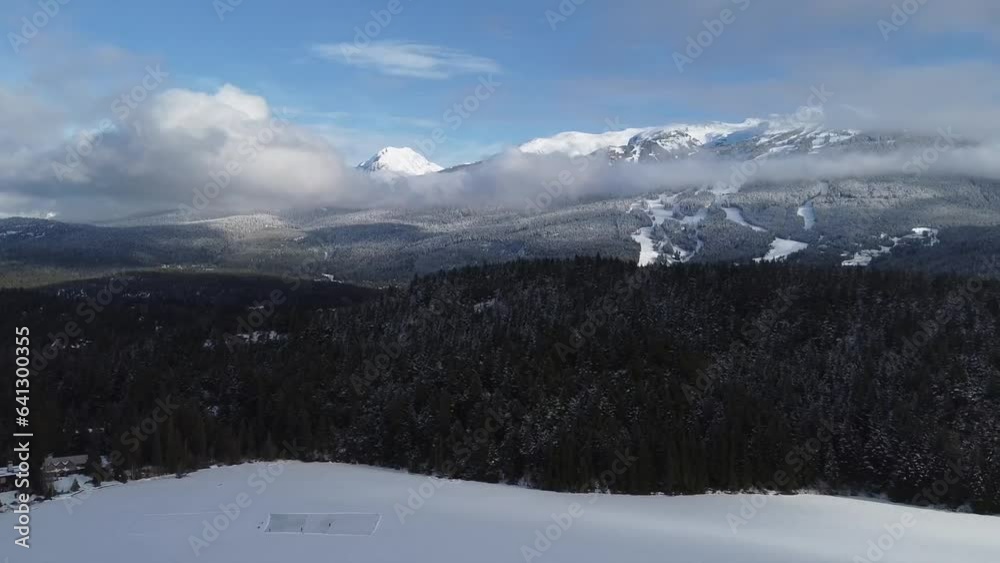 Frozen Lake With Surrounding Pine Forest And Snow-covered Mountain Range During Winter In Whistler, Canada. aerial pullback Frozen Lake With Surrounding Pine Forest And Snow-covered Mountain Range During Winter In Whistler, Canada. aerial pullback