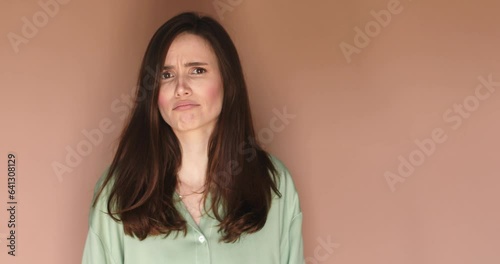 Pensive puzzled young girl wear green shirt thinking isolated on beige color background in studio. Thoughtful woman thinks deeply chooses or ponders plan and not sure. 