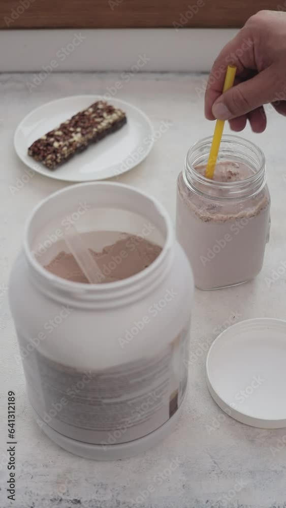 Male hand with a straw mixing whey protein powder in a glass jar with milk, process of making protein drink smoothie, sport nutrition, vertical video Male hand with a straw mixing whey protein powder in a glass jar with milk, process of making protein drink smoothie, sport nutrition, vertical video
