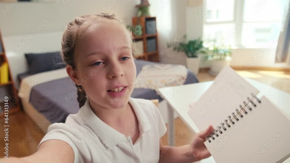 POV shot of small girl talking during video call with her tutor and showing notebook to camera standing in kids room POV shot of small girl talking during video call with her tutor and showing notebook to camera standing in kids room