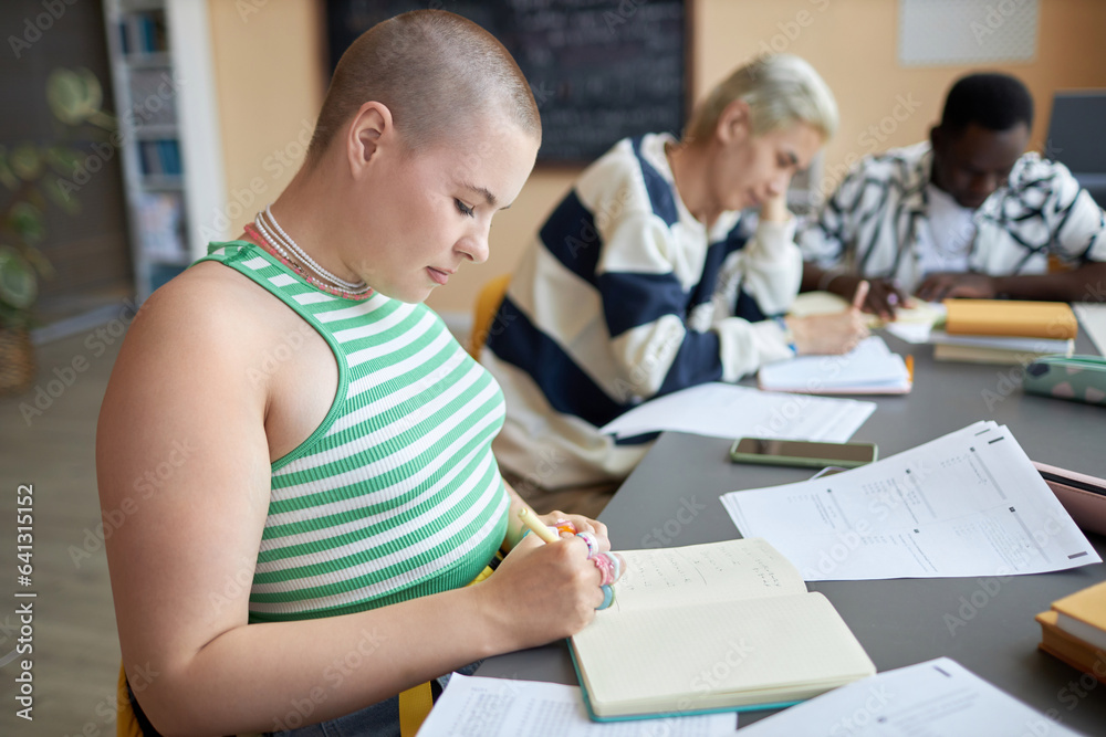 Obraz premium Side view of serious young woman sitting by desk and thinking of answer to one of test questions before writing it down in copybook