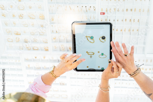 Luxury jewelry store concept. Jewelry boutique. View froma above of females hands with tablet choosing golden ring in the online store on display in jewelry store. Online shopping with a tablet. photo