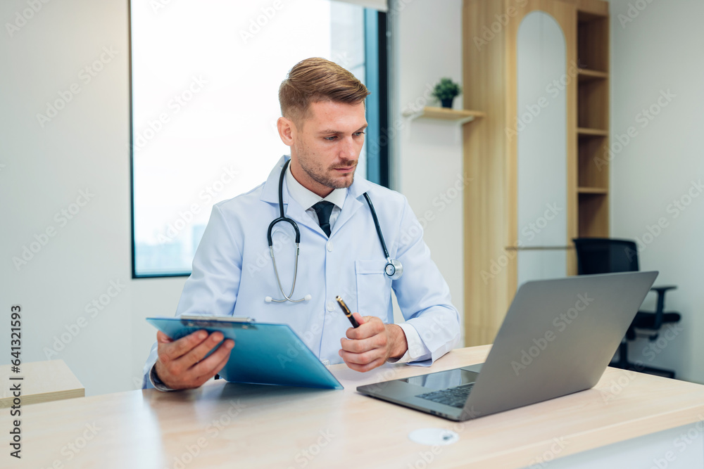 Male Doctor expert wearing white coat using laptop and reading clipboard report at work in hospital. Male Doctor expert wearing white coat using laptop and reading clipboard report at work in hospital.