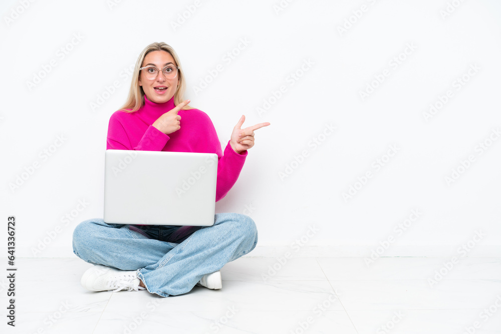 Young caucasian woman with laptop sitting on the floor surprised and pointing side Young caucasian woman with laptop sitting on the floor surprised and pointing side