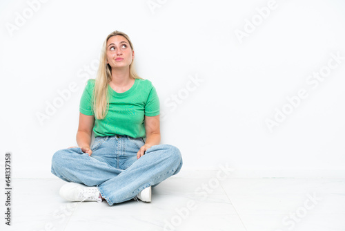 Young caucasian woman sitting on the floor isolated on white background and looking up