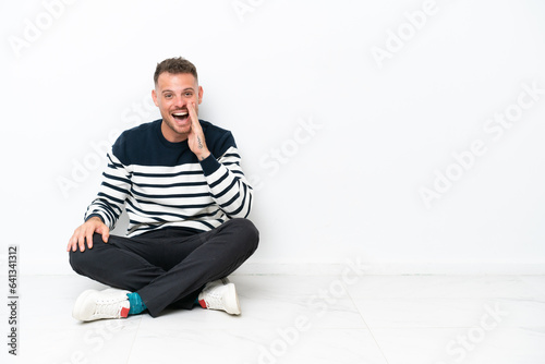 Young man sitting on the floor isolated on white background shouting with mouth wide open