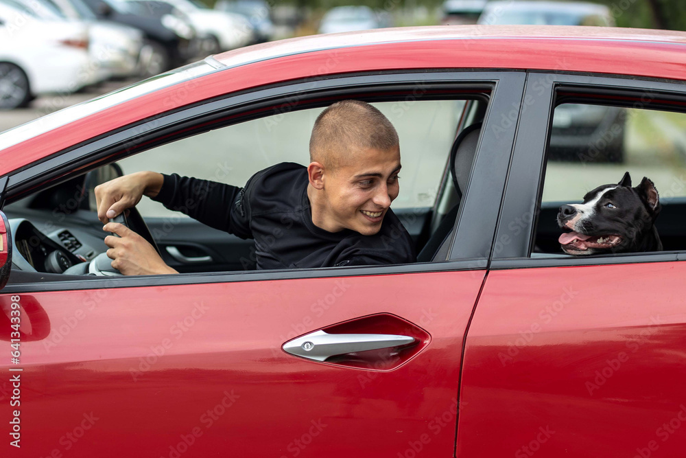 A young man driving a car has his head turned toward his dog, chatting cheerfully with him.