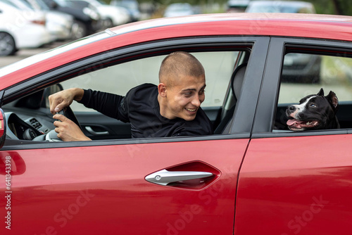 A young man driving a car has his head turned toward his dog, chatting cheerfully with him.