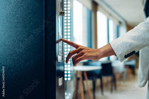 Close up view of woman's finger pushing number button on keyboard of snack vending machine. Self-used technology and consumption concept 