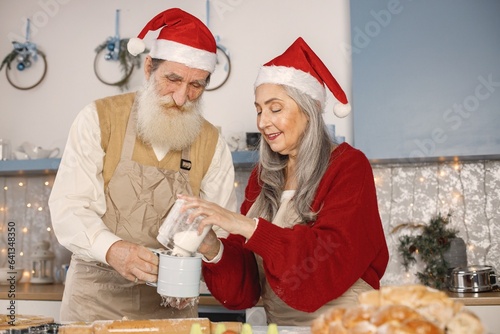 Senior couple in christmas red hats cooking in kitchen