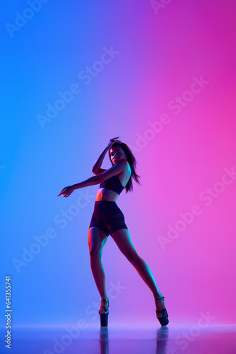 Beautiful female dancer wearing bodysuit and heels while performing pole dance tricks in colorful neon light