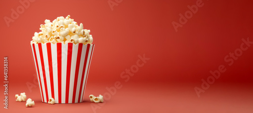 Popcorn in red and white striped cardboard bucket on red background, copy space for advertisement