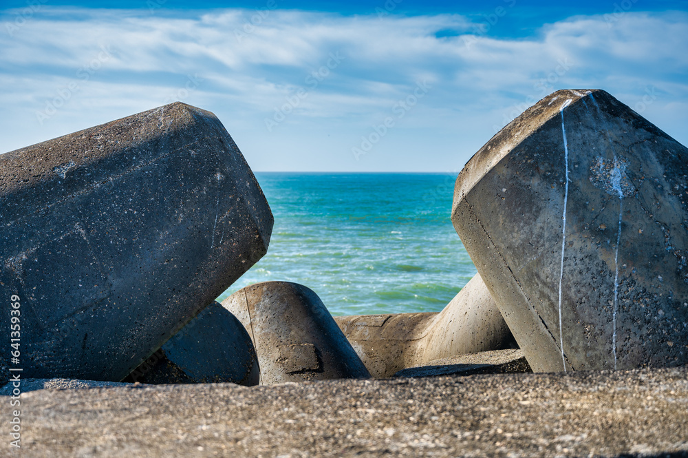 Concrete breakwater blocks protecting the coast from the ocean waves under a hazy sky. Concrete breakwater blocks protecting the coast from the ocean waves under a hazy sky.