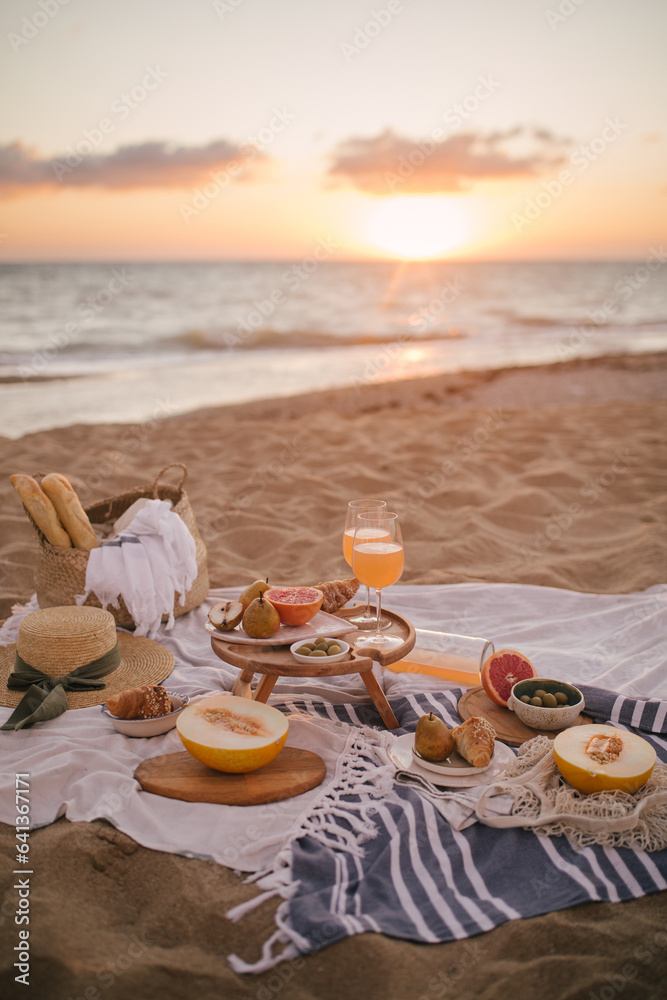 Beautiful tasty picnic with lemonade, fresh fruits and croissants on a beach at sunset.