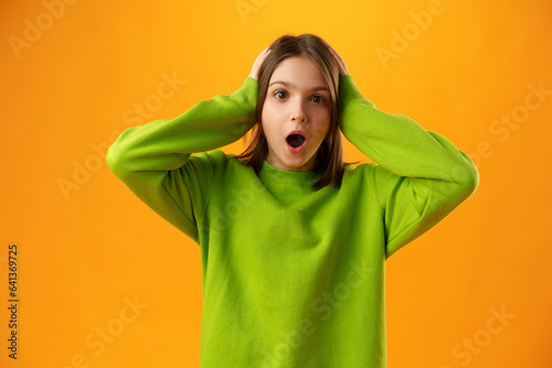 Surprised amazed teen girl against yellow background in studio