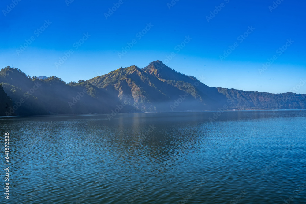 The hills on the shores of Lake Batur, Kintamani, Bali, in the morning, bathed in the warm rays of the sun as they gently touch the surface of the lake