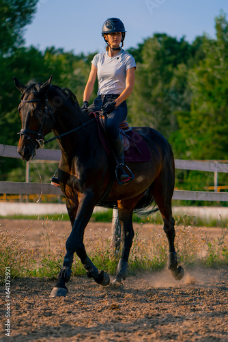 A horsewoman dressed in a helmet rides her beautiful black horse in a horse riding arena during a horseback ride