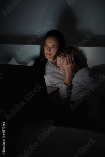 Mother helping sleepy son to do homework in darkness