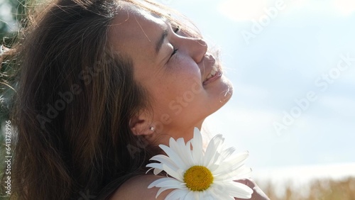 Happy woman with big chamomile in her hand in summer field. Carefree girl enjoys freedom and tranquility in the countryside during her vacation. The concept of rest or relaxation and happiness or photo