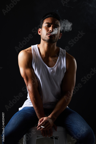 Smoking portrait, sexy man and chair in studio in fitness, beauty aesthetic and strong sensual fashion. Art, body and male model with muscle, cigarette and jeans on black background in dark lighting.