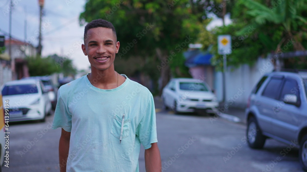 One cheerful young Brazilian man waving hello to neighbor walking in street. Joyful South American individual greeting friend with hand