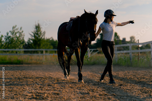 A helmeted rider leads her beautiful black horse by the harness in the riding arena during a horseback ride © Guys Who Shoot