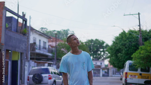 One pensive young black Brazilian man looking up at sky in contemplative and thoughtful expression. South American 20s person gazing at neighborhood